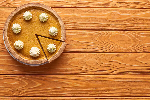 top view of delicious, cut pumpkin pie with whipped cream on orange wooden table