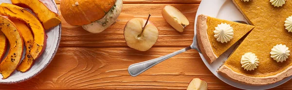 生と焼きカボチャの近くにホイップクリームとおいしいカボチャのパイのパノラマショット オレンジの木のテーブルの上にリンゴをカット — ストック写真