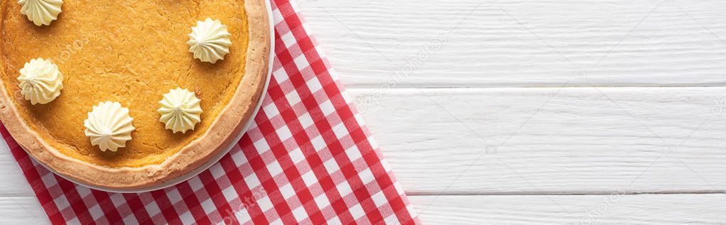 panoramic shot of tasty pumpkin pie with whipped cream and checkered napkin on white wooden table