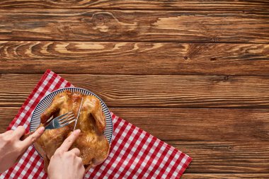cropped view of woman cutting roasted turkey on red plaid napkin on wooden table clipart