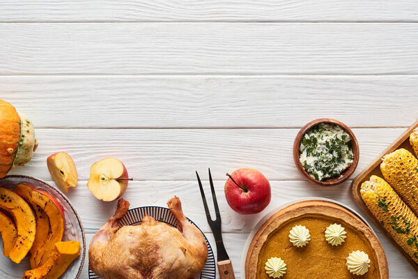 верхний вид жареной индейки, тыквенный пирог и жареная кукуруза подается на белом деревянном столе с красной клетчатой салфеткой
