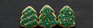 flat lay with delicious glazed Christmas tree cookies on black wooden table, panoramic shot clipart