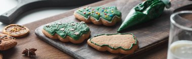 selective focus of baked Christmas cookies near pastry bag on wooden table, panoramic shot clipart