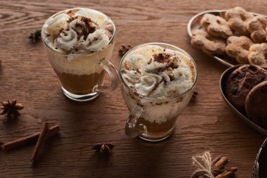 Baharat ve kurabiyelerin yanındaki ahşap masada kremalı Noel kakaosu.