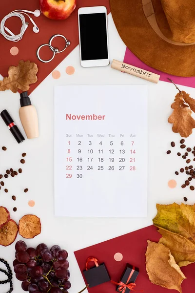 十一月的日历页接近帽子 甜甜圈 化妆品 咖啡粒和木制块 上面有十一月的题词 白色隔断 — 图库照片