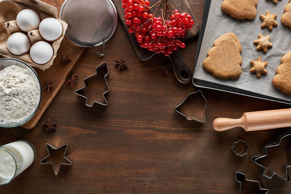 top view of Christmas cookies near ingredients, dough molds and viburnum on wooden table