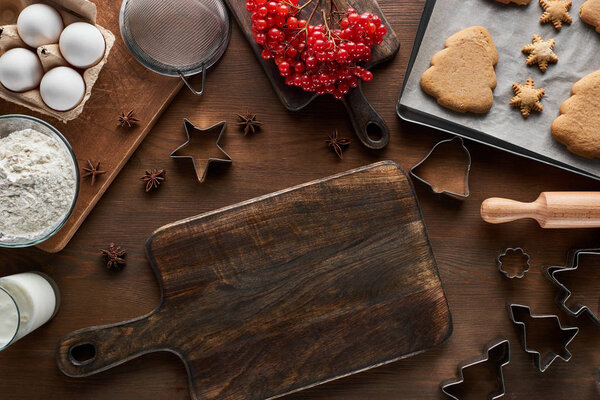 top view of empty cutting board near Christmas cookies, ingredients, dough molds and viburnum on wooden table