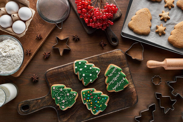top view of glazed Christmas cookies near ingredients, dough molds and viburnum on wooden table