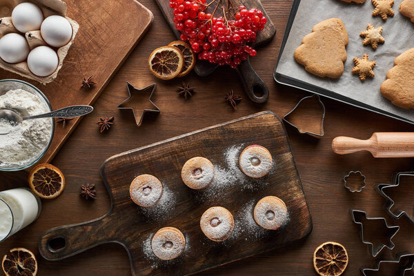 top view of Christmas cookies near ingredients, dough molds and viburnum on wooden table