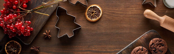 top view of chocolate cookies near Christmas dough molds, viburnum and spices on wooden table with copy space, panoramic shot