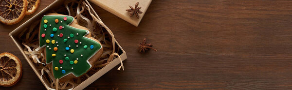 top view of Christmas tree cookie in box near dried citrus and anise at wooden table, panoramic shot