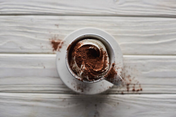 selective focus of Christmas cacao in mug with whipped cream and cacao powder on white wooden table