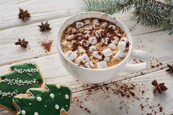 cacao with marshmallow in mug on white wooden table with fir branch and Christmas cookies