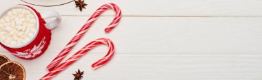 top view of christmas candy canes and cup of cocoa with marshmallows on white wooden table  clipart