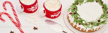 top view of christmas pie with rosemary, candy canes and two cups of cocoa with marshmallows on white wooden table   