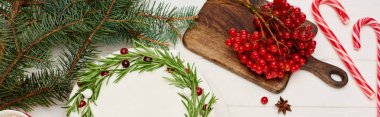 Beyaz ahşap masa üzerinde ladin dallarıyla noel pastası ve viburnum üzümlerinin üst görüntüsü.