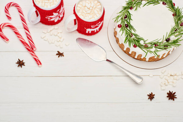 top view of two cups of cocoa with marshmallows and christmas pie with icing on white wooden table 