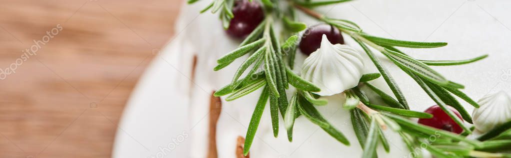 close up of christmas cake with icing, rosemary and cranberries on wooden table 