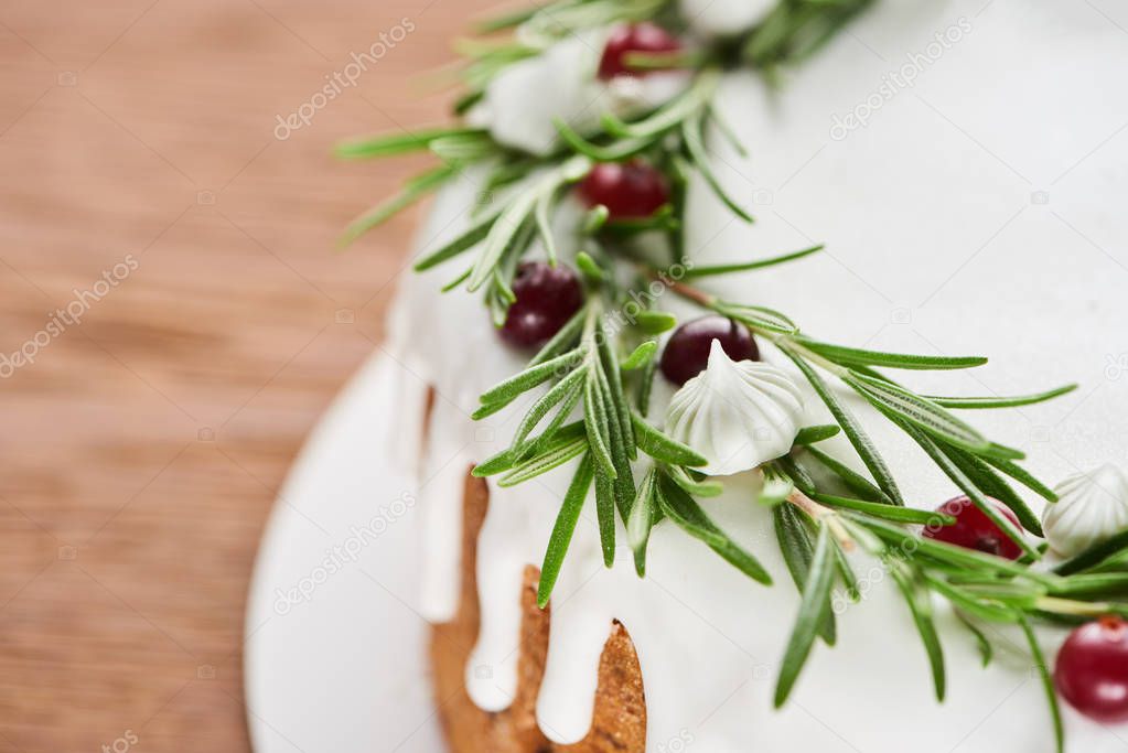 christmas pie with white icing, rosemary and cranberries on wooden table 