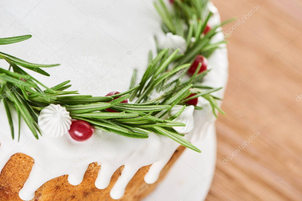 close up of christmas pie with white icing, rosemary and cranberries on wooden table 