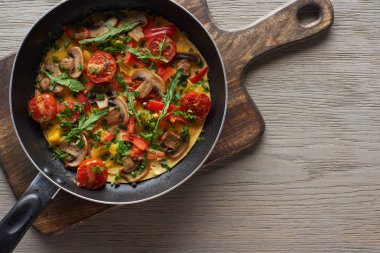 Tahtadaki tavada sebzeli ve yeşillikli lezzetli omlet manzarası. 