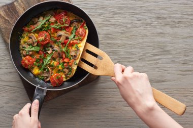 Kızartma tavasında mantarlı, domatesli ve yeşillikli omlet pişiren bir kadın.