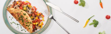 Tabağın üst görüntüsü, sarılı omlet, beyaz masa üzerinde sebzeler, biber, domates ve brokoli.