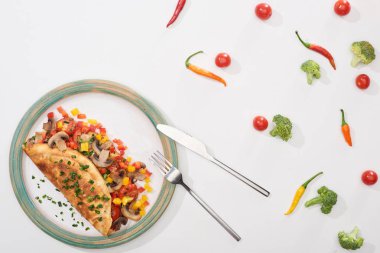 top view of plate with homemade wrapped omelet with vegetables on white table with chili peppers, tomatoes and broccoli clipart