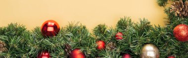 Sarı zemin üzerinde kırmızı ve altın takılar olan noel ağacı dalının en üst görüntüsü, panoramik çekim