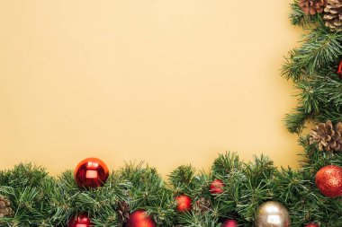 Sarı zemin üzerinde kırmızı ve altın takılar olan noel ağacı dalının en üst görüntüsü