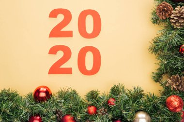 2020 sayılı kağıdın en üst görüntüsü, sarı zemin üzerinde takılar olan noel ağacı dalına yakın.