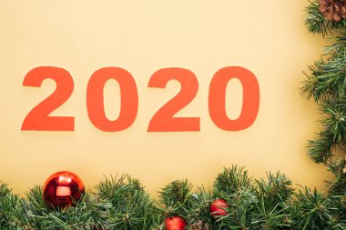 2020 sayılı kağıdın en üst görüntüsü, sarı zemin üzerinde takılar olan noel ağacı dalına yakın.