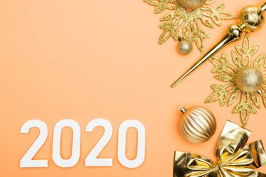Turuncu arka planda, altın noel süslemesi yakınlarında beyaz 2020 sayısının üst görünümü