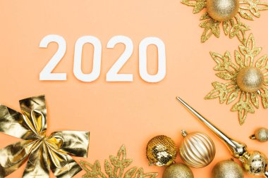 Turuncu arka planda, altın noel süslemesi yakınlarında beyaz 2020 sayısının üst görünümü