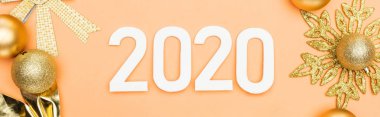 Turuncu arka planda altın noel süslemesi yakınlarındaki beyaz 2020 rakamlarının üst görünümü, panoramik çekim