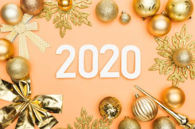 Turuncu arkaplanda altın noel süslemesi çerçevesinde beyaz 2020 sayısının üst görünümü