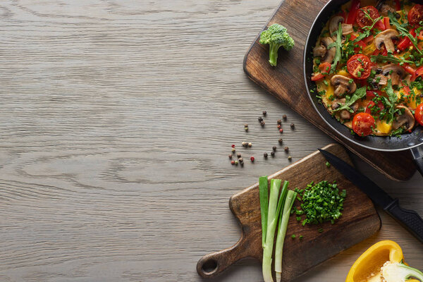 вид сверху на домашний омлет в сковороде с ингредиентами и ножом на столе
