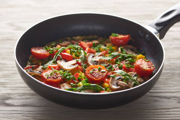 вкусный домашний омлет с овощами и зеленью на сковородке на деревянном столе
