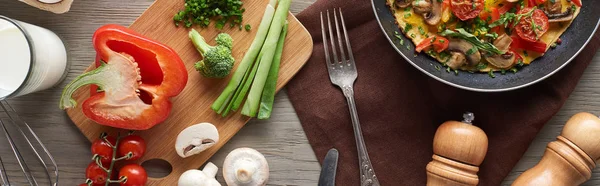 top view of homemade omelet in frying pan with healthy ingredients on table
