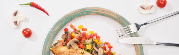 top view of plate with yummy wrapped omelet with vegetables on white table with ingredients, fork and knife 