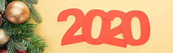 top view of paper 2020 numbers near christmas tree branch with baubles on yellow background, panoramic shot