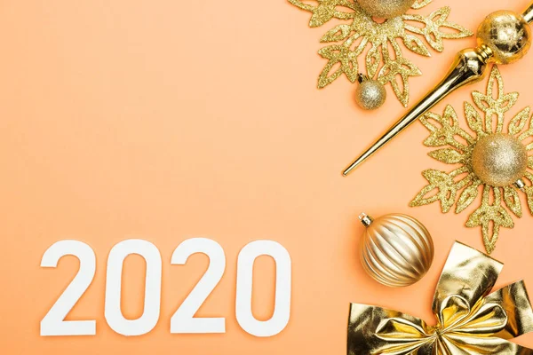 Turuncu arka planda, altın noel süslemesi yakınlarında beyaz 2020 sayısının üst görünümü