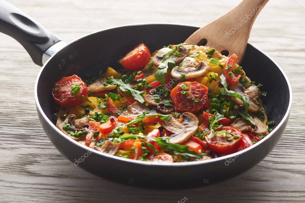 homemade omelet with vegetables and greens in frying pan with wooden shovel