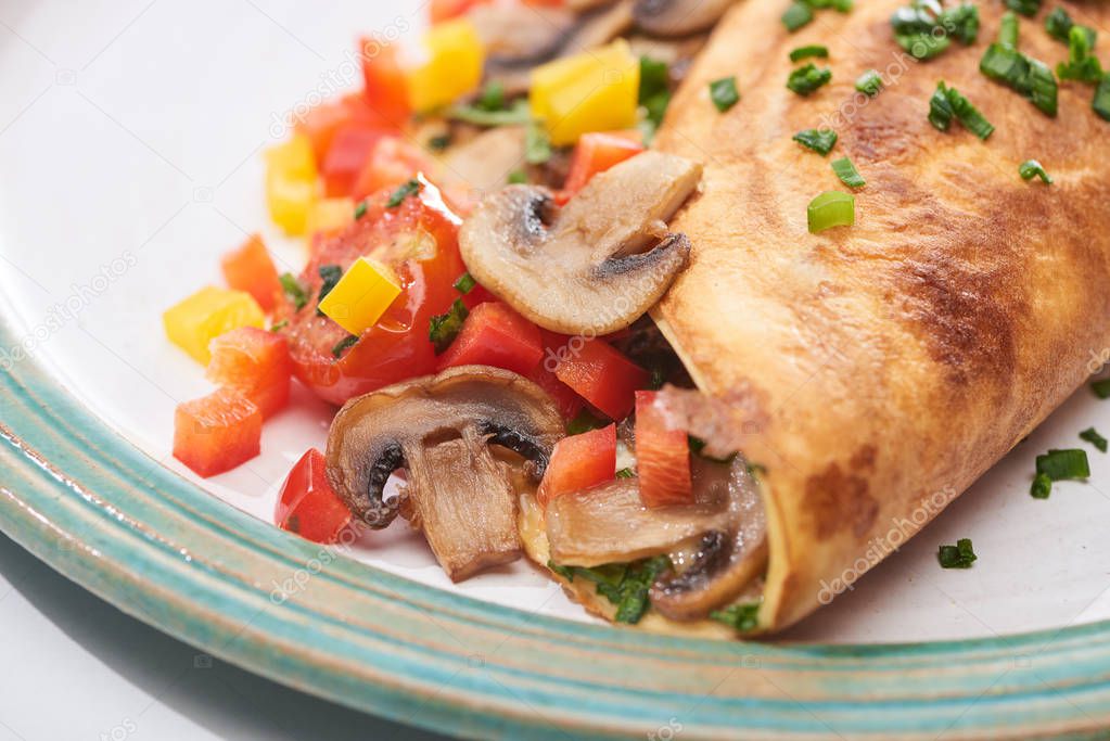 close up of yummy wrapped omelet with mushrooms and peppers on plate