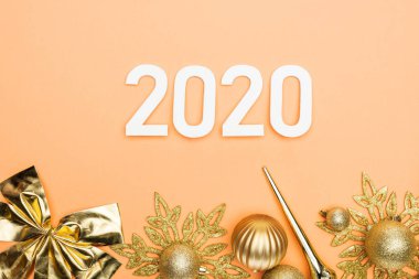 Beyaz 2020 rakamlarının üst görüntüsü ve turuncu arka planda altın noel süslemesi