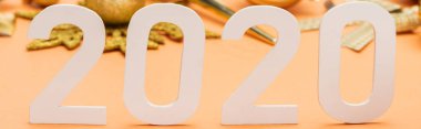 Turuncu arka planda altın noel süslemesi önünde beyaz 2020 sayısının seçici odak noktası, panoramik çekim