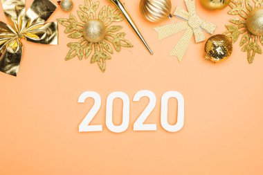 Turuncu arka planda, altın noel süslemesi yakınlarındaki 2020 sayının en üst görüntüsü