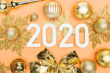 Turuncu arka planda altın noel süslemesi üzerine beyaz 2020 rakamlarının üst görünümü