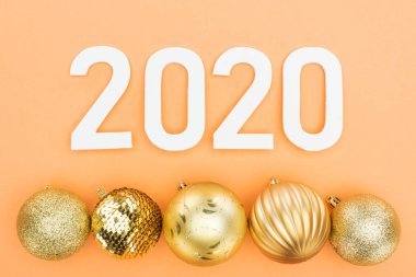 Turuncu arka planda altın noel mücevherlerinin yanındaki beyaz 2020 rakamının en üst görüntüsü