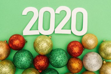 Beyaz 2020 rakamlarının üst görünümü yeşil arka planda çok renkli Noel mücevherleri yanında